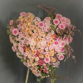 Large heart-shaped standing arrangement of pink and peach roses on an easel