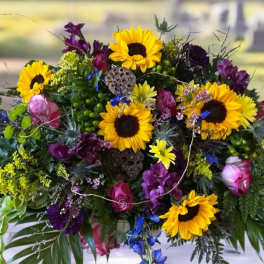 Colorful floral casket spray with sunflowers, roses, and purple blooms