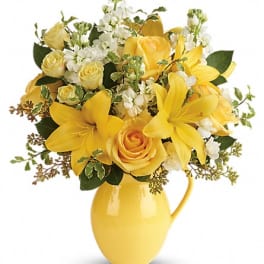 Yellow roses and lilies in a yellow pitcher vase