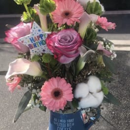 Pink mixed flower bouquet in a blue mug with a birthday card.