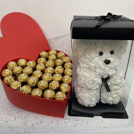 Heart-shaped candy box and a white rose teddy bear in a display case