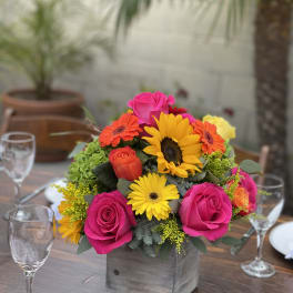 Bright mixed bouquet in a square wooden vase on a table
