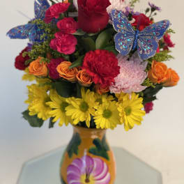 Mixed bouquet of roses, carnations, and daisies in a painted vase with butterfly picks