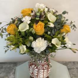 Bouquet of yellow roses, white calla lilies, and white carnations in a patterned vase