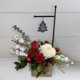 Red roses and white blooms in a rustic wooden container with a hanging tree ornament