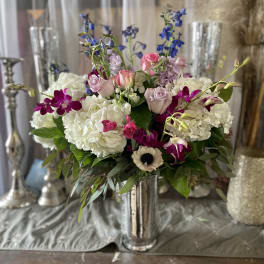 Mixed bouquet of white hydrangeas, pink roses, and purple orchids in a silver vase