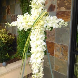 White floral cross on an easel with lilies and orchids