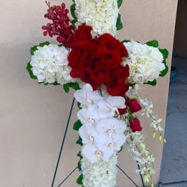 Cross-shaped floral tribute with red roses, white hydrangeas, and white orchids