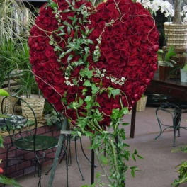 Heart-shaped red rose arrangement on a stand with trailing greenery