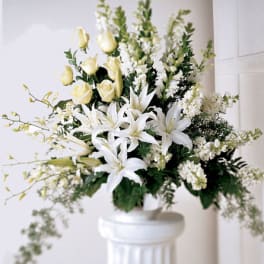 White lilies and pale yellow roses in a white pedestal vase