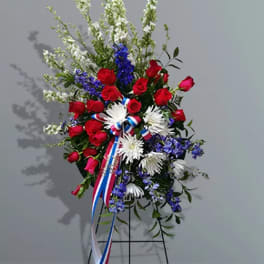 Standing floral spray with red roses, white daisies, and blue flowers on an easel