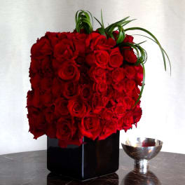 Red rose arrangement in a black vase with curled green leaves