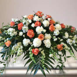 Orange and white floral casket spray with cascading greenery
