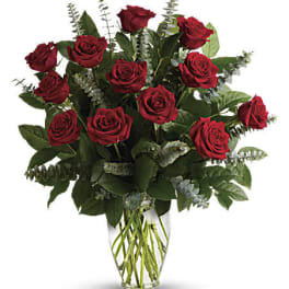 Red roses arranged in a clear glass vase with greenery