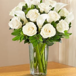 White roses and calla lilies arranged in a clear glass vase