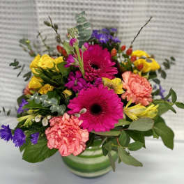 Bright mixed bouquet in a green-striped vase with pink, yellow, and purple flowers