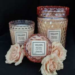 Three rose-scented candles with pale pink roses on a black background
