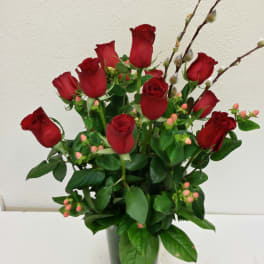 Red roses arranged in a clear glass vase with berry sprigs