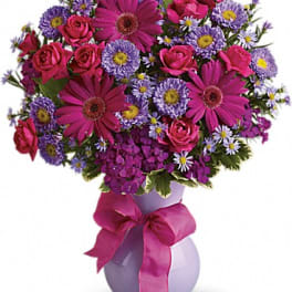 Bouquet of pink and purple flowers in a lavender vase with a ribbon