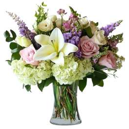 Bouquet of white lilies, pink and cream roses, and purple flowers in a glass vase