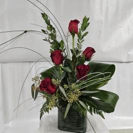 Red roses arranged in a square glass vase with tall greenery