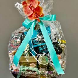 Gift basket wrapped in clear cellophane with a turquoise ribbon and orchid topper