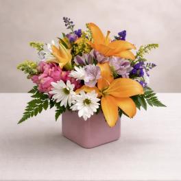 Mixed bouquet of orange lilies, pink flowers, and white daisies in a pink vase
