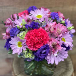Mixed bouquet of pink, purple, and lavender flowers in a glass vase