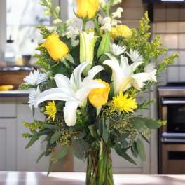 Yellow roses and white lilies in a clear glass vase