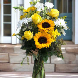 Yellow roses and sunflowers in a clear glass vase with white daisies