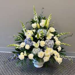 White and pale blue floral arrangement in a white urn vase