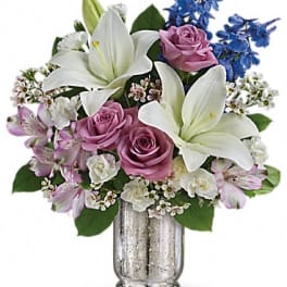 Bouquet of white lilies, pink roses, and blue flowers in a silver vase