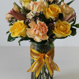 Yellow roses and peach carnations in a clear glass vase with a yellow ribbon bow
