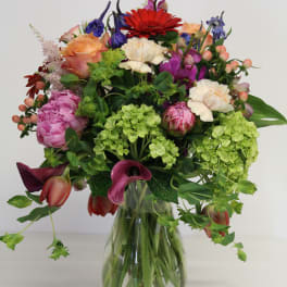 Mixed bouquet of pink, peach, red, purple, and green flowers in a clear glass vase