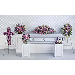 Funeral casket surrounded by pink and purple floral sprays