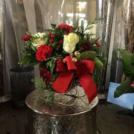 Red and white floral arrangement with a large red bow in a decorative vase