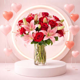 Red roses and pink lilies in a clear glass vase with heart balloons