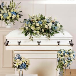 White casket with blue and cream floral sprays and arrangements