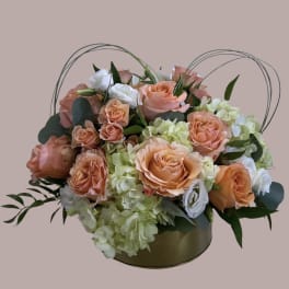Peach roses and white blooms in a round gold box