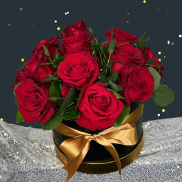 Red roses arranged in a black round box with a gold ribbon
