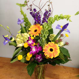 Colorful mixed bouquet in a clear glass vase with orange gerberas and purple blooms