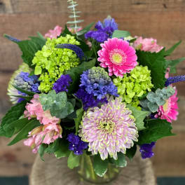 Colorful bouquet with pink gerbera daisies, green hydrangeas, and purple blooms in a glass vase