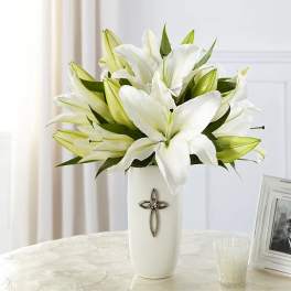 White lilies arranged in a tall white vase with a cross emblem