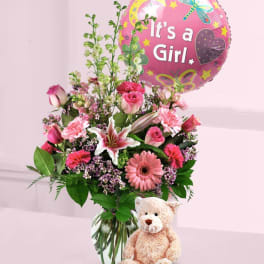 Pink mixed flower bouquet in a glass vase with a girl balloon and teddy bear