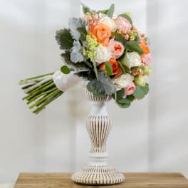 Bouquet of peach, white, and pink roses in a white pedestal vase