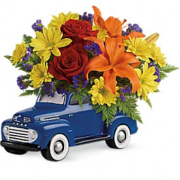 Flower arrangement in a blue toy truck with red roses, orange lilies, and yellow daisies