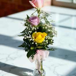 Pink, lavender, and yellow roses in a clear glass vase with a pink ribbon