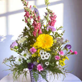 Mixed bouquet in a white woven basket with yellow, pink, purple, and white flowers