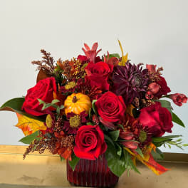 Red roses and autumn flowers in a red glass vase with a small pumpkin