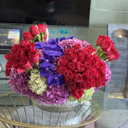 Large bouquet of red roses, purple orchids, and hydrangeas in a glass bowl vase